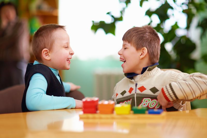 Two boys laugh together while playing with blocks at a table.