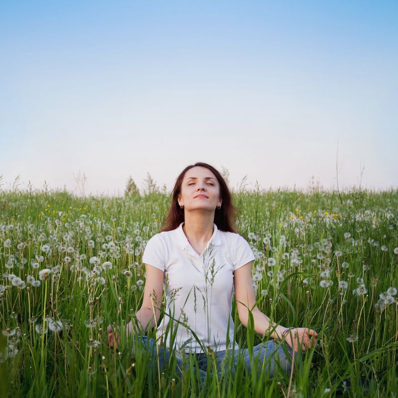 A woman sits with her eyes closed in a field of tall grass.