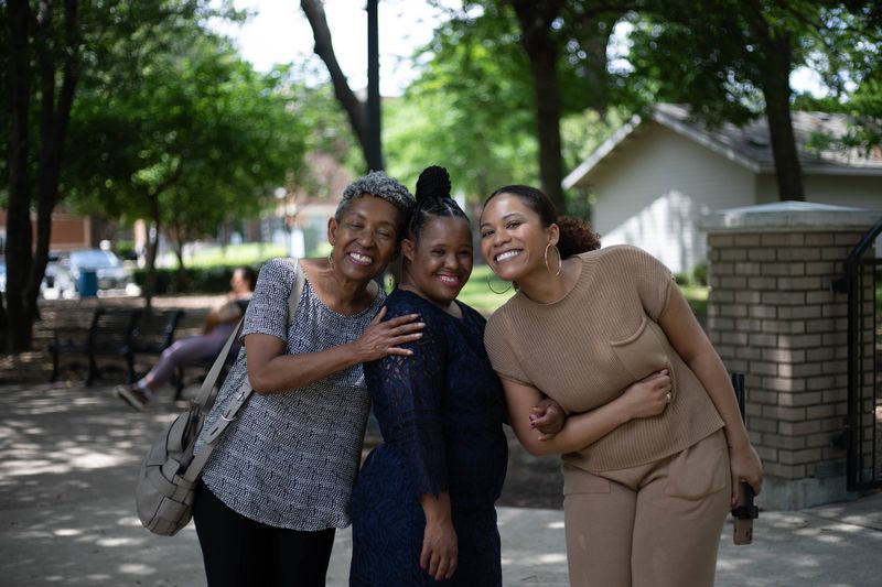 Three friends lean in close and smile on a sunny day.