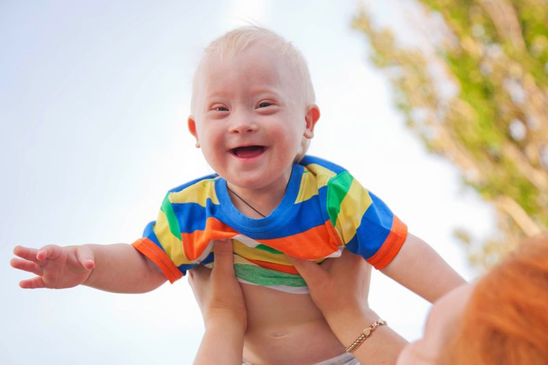 A laughing toddler is lifted up in the sunshine.