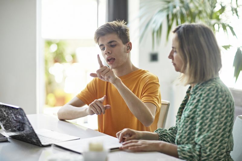 A young man signs during a conversation at a table.