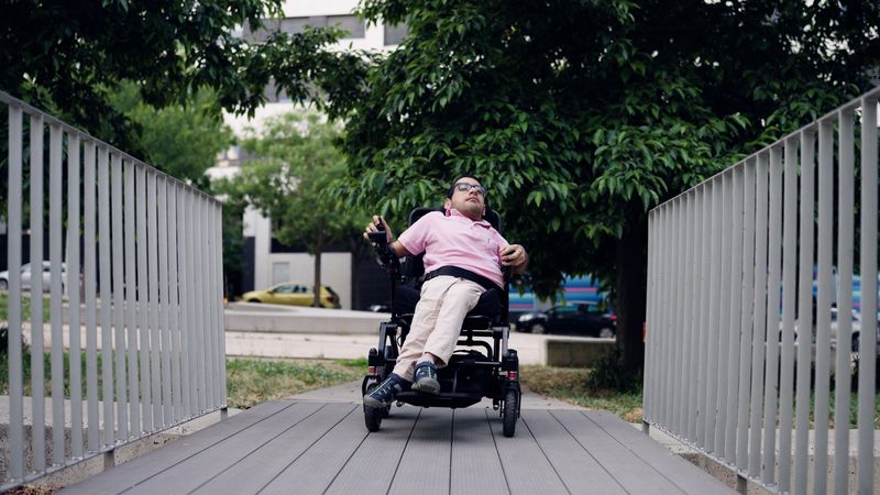 A woman in a power wheelchair crosses a wooden bridge.