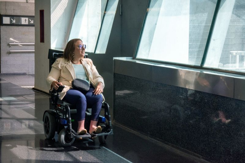 A woman in a power wheelchair moves through a bright office lobby.