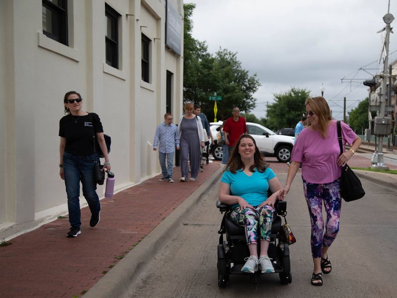 Friends walk down a city sidewalk, one in a power wheelchair.