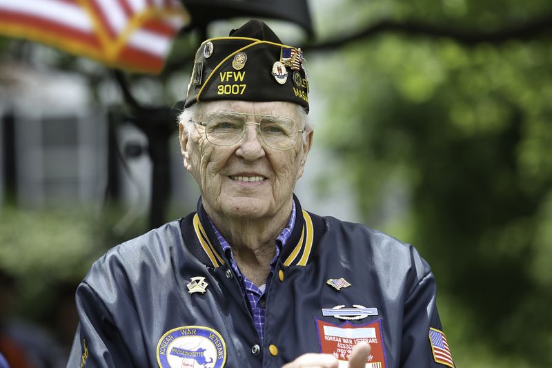 A veteran in a VFW cap and jacket smiles outdoors.